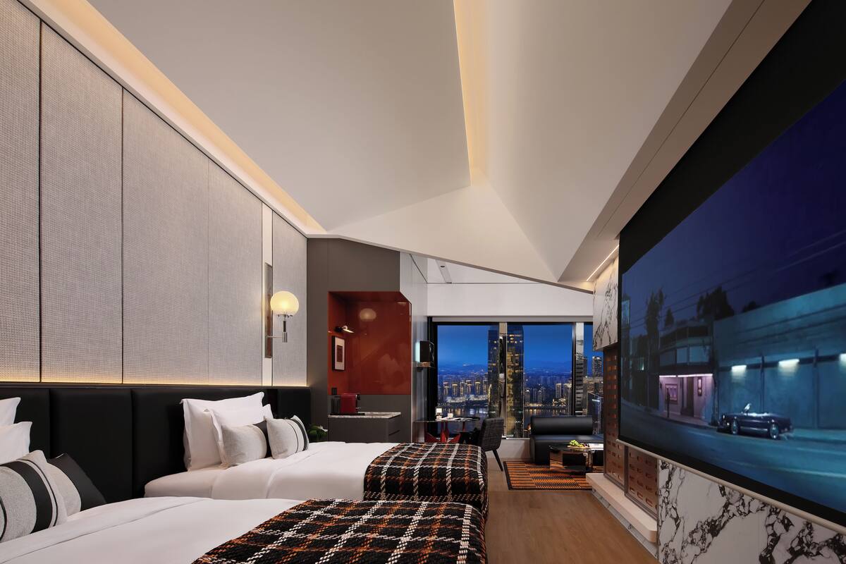 A modern hotel room with a large bed, a smaller bed, a TV, a city view, and a desk with a chair.