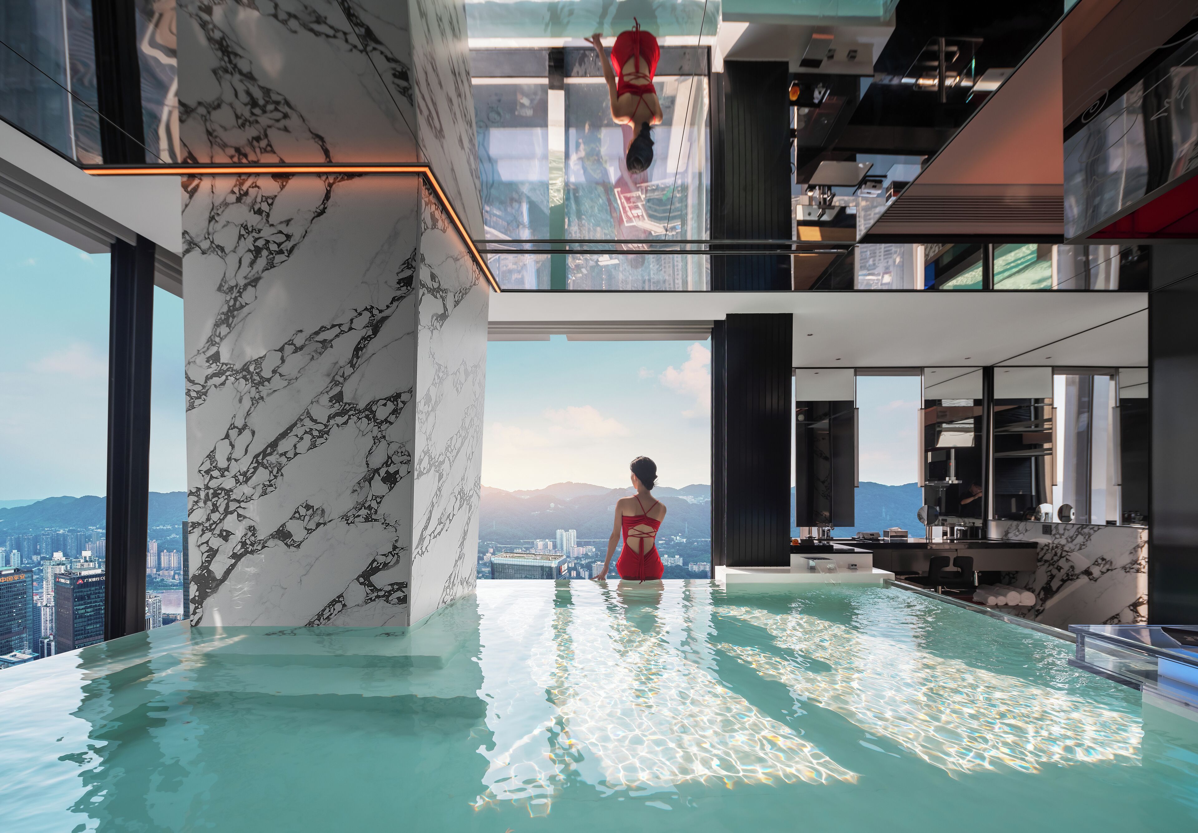 A modern indoor infinity pool with a city view, marble walls, and a red swimsuit.