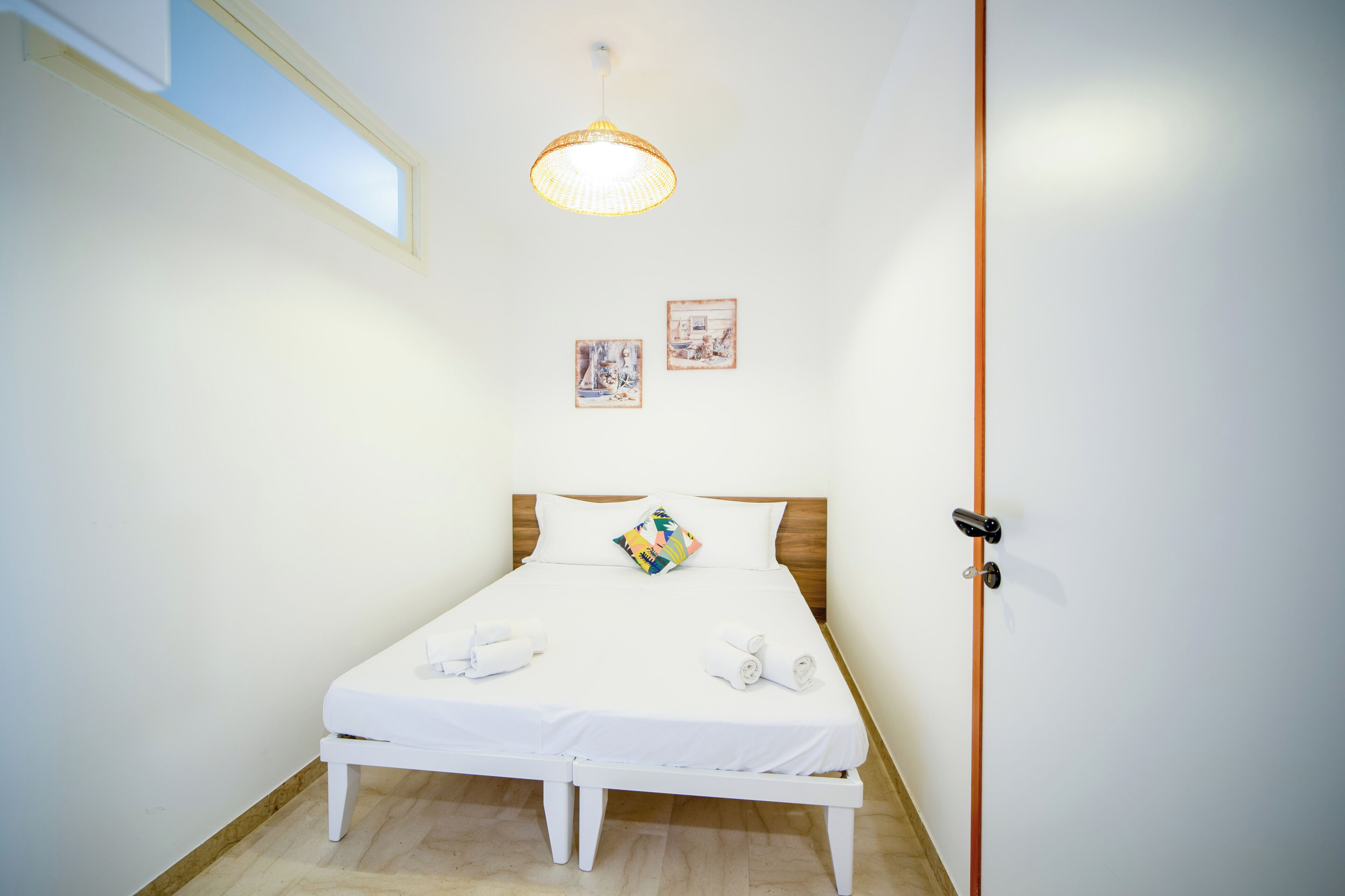 Een opgemaakt bed met wit beddengoed en twee kussens, een klein nachtkastje en een wandlamp.