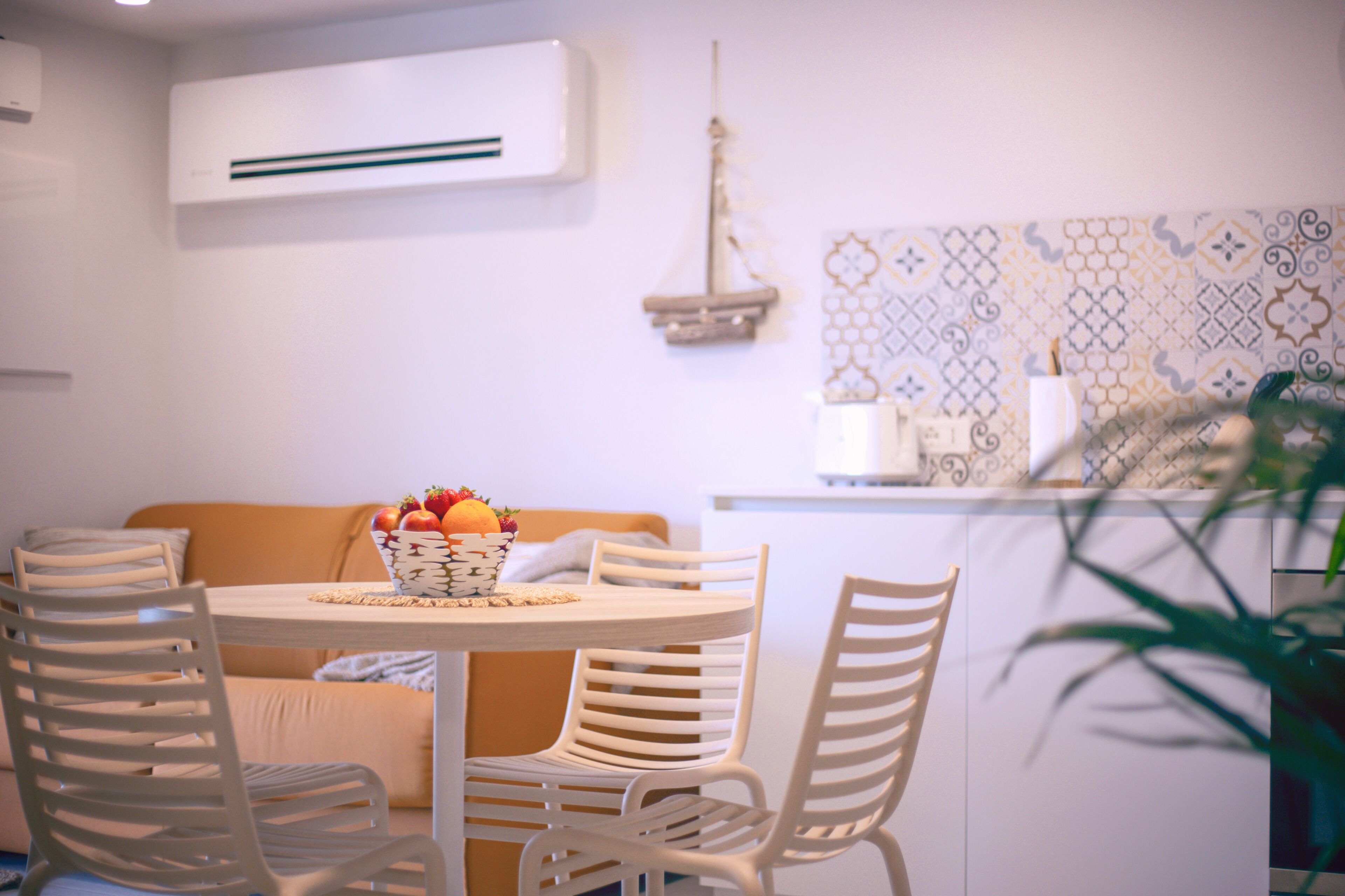 A dining area with a round table, four chairs, a basket of fruit, and a patterned wall.