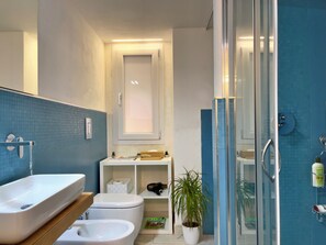 Un bagno con lavandino bianco, WC, bidet, zona doccia e mobiletto.