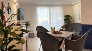 A dining area with a table, chairs, a television, and a window with curtains. - Marina Beach Apartments (Alcamo)