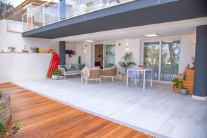 Patio esterno moderno con pavimento in legno, mobili bianchi e piante in vaso.