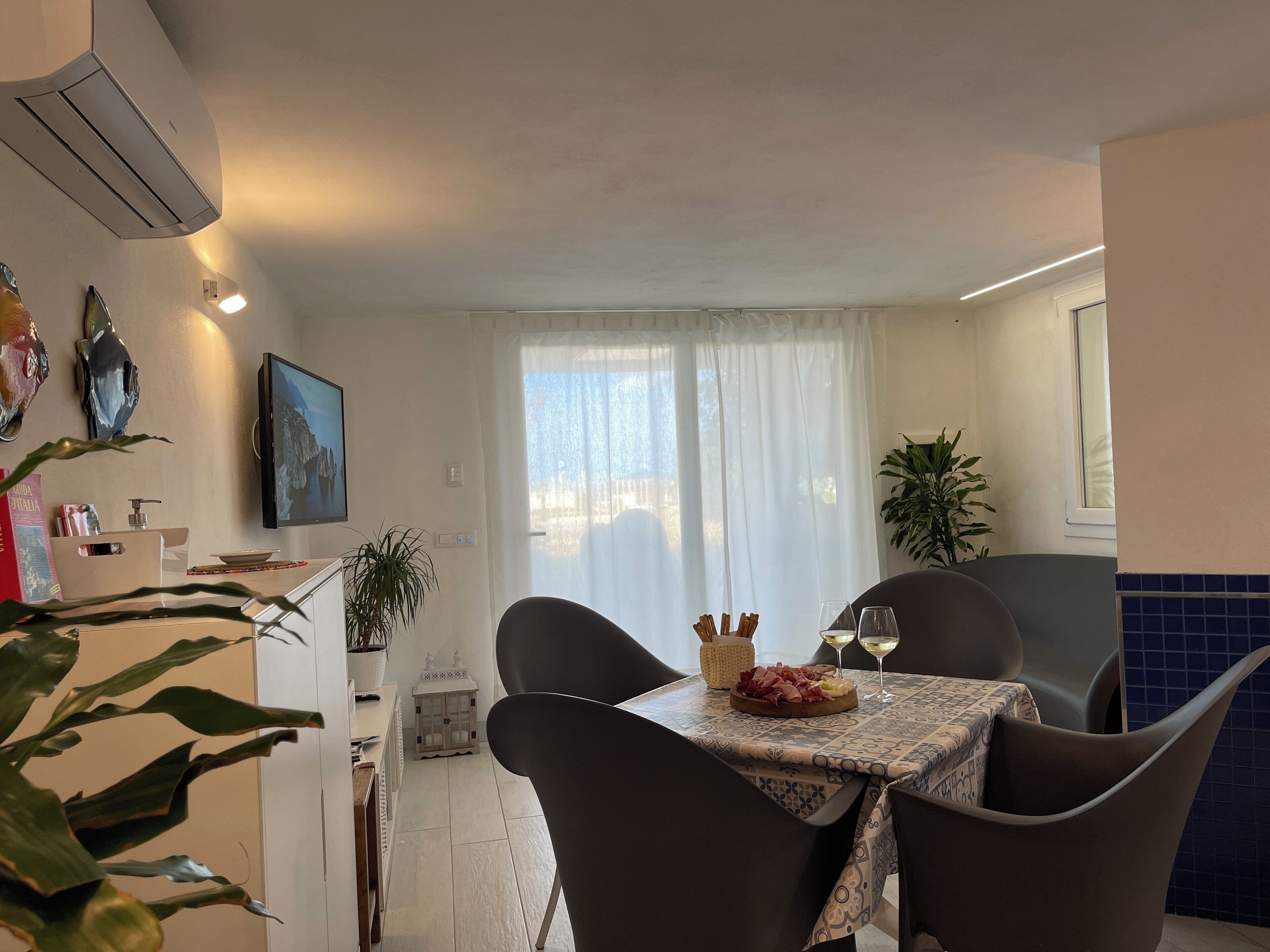 A dining area with a table set for two, a potted plant, and a window with curtains.