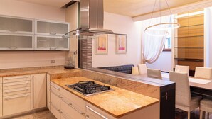 Een moderne keuken met een ingebouwd gasfornuis, een rvs afzuigkap en een eethoek met een glazen tafel en stoelen.