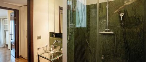 A modern bathroom with a glass-enclosed shower, a glass sink, and a marble wall.