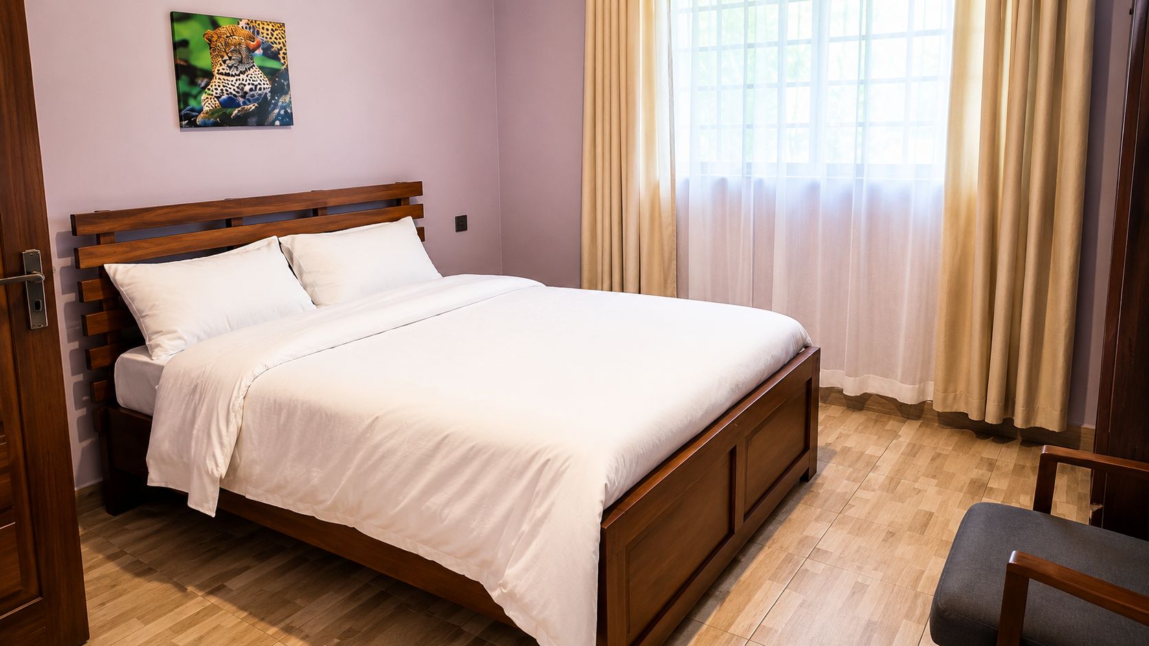 A neatly made bed with a wooden headboard, a window with curtains, and a chair.