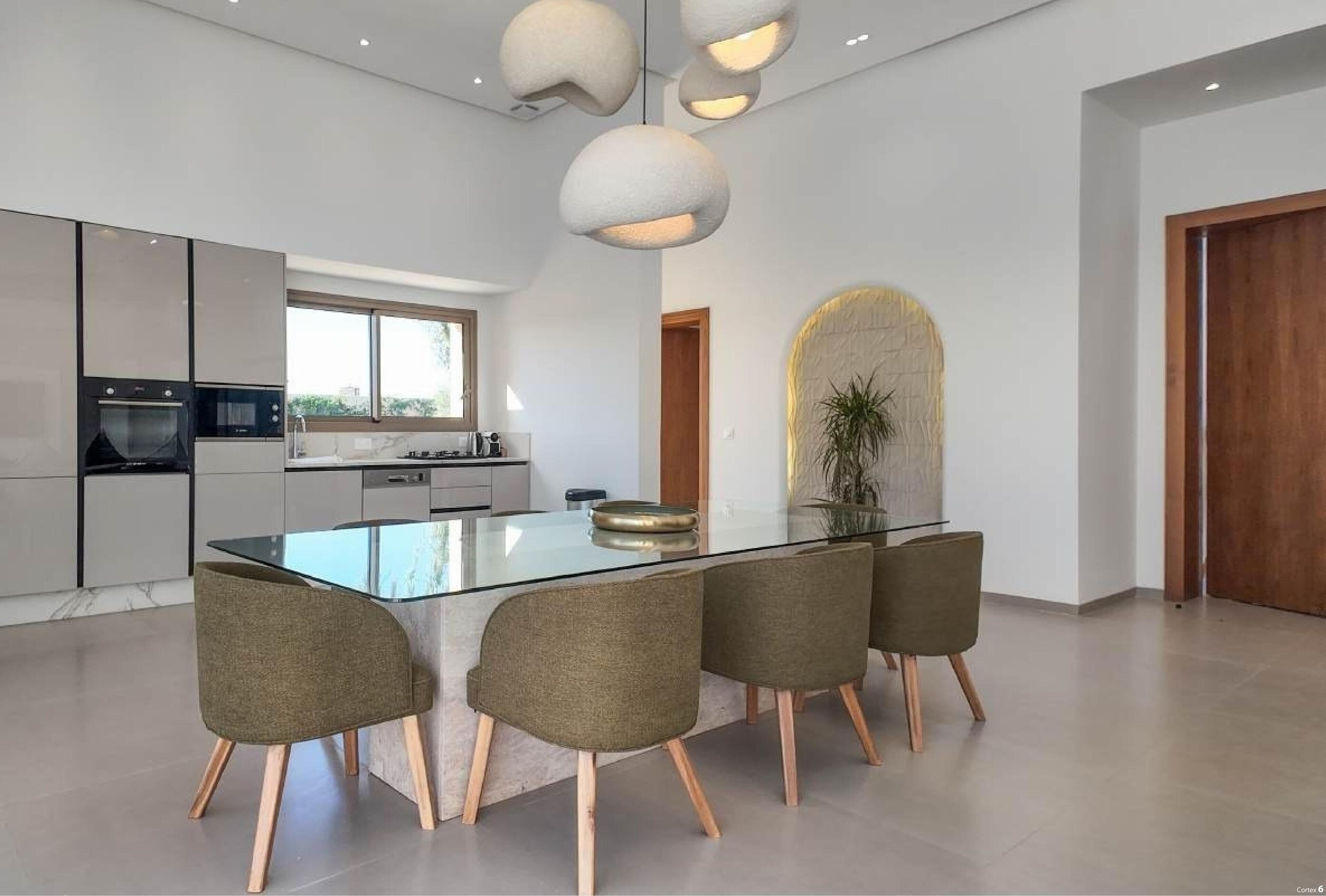 Cocina moderna con isla de vidrio, cuatro sillas e iluminación colgante.