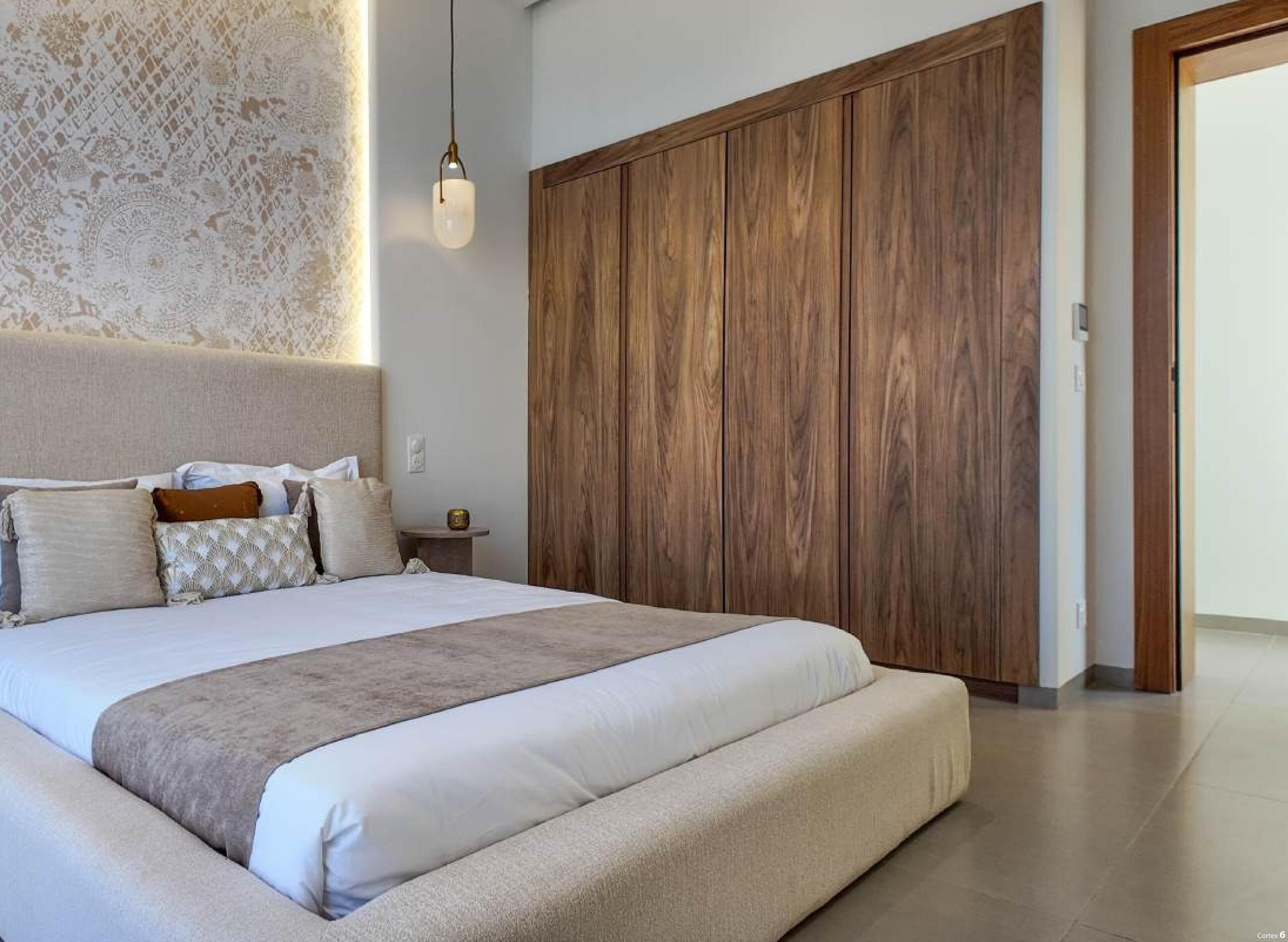 A bedroom with a large bed, a wooden wardrobe, and a patterned wall.