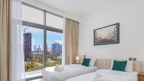 A hotel room with two beds, a large window with a view of a cityscape, a framed picture on the wall, and a nightstand with a lamp. - LUX The Hadley JVC Suite (Dubai)