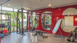 A modern gym with various exercise equipment, large mirrors, and a view of palm trees outside. - LUX The Hadley JVC Suite (Dubai)