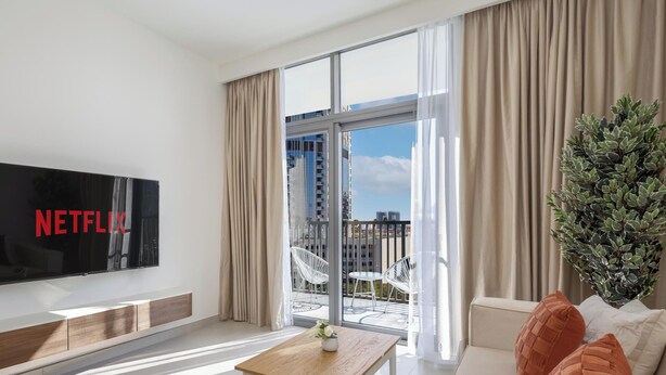 A modern living room with a large flat-screen TV displaying "NETFLIX," a balcony with white chairs, and a potted plant. - LUX The Hadley JVC Suite (Dubai)