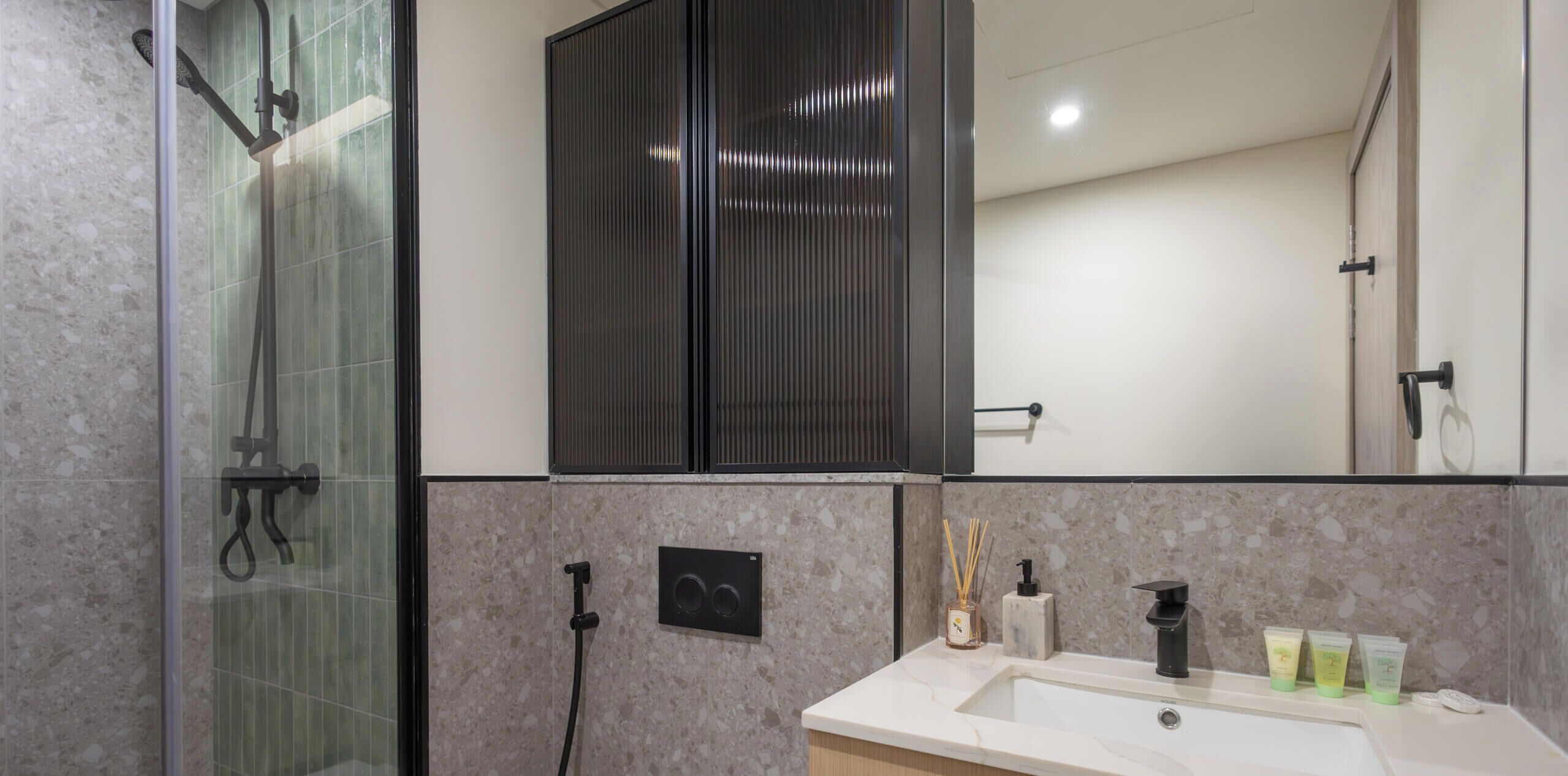 Een moderne badkamer met een douchecabine van glas, een grote spiegel en een wastafelgedeelte betegeld met marmer.