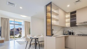 A modern kitchen with a built-in stove, a sink, and a dining area with a table and chairs. - LUX The Hadley JVC Suite (Dubai)