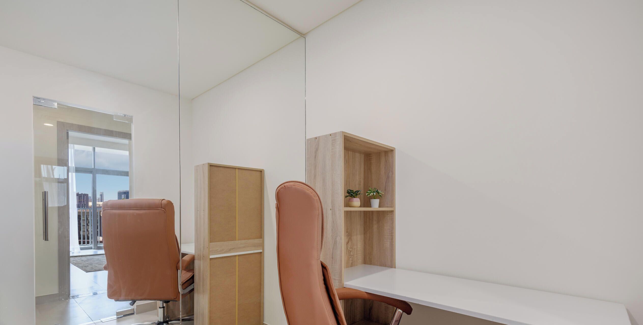 Un espacio de oficina moderno con dos sillones de cuero, un escritorio blanco y una estantería de madera con plantas.