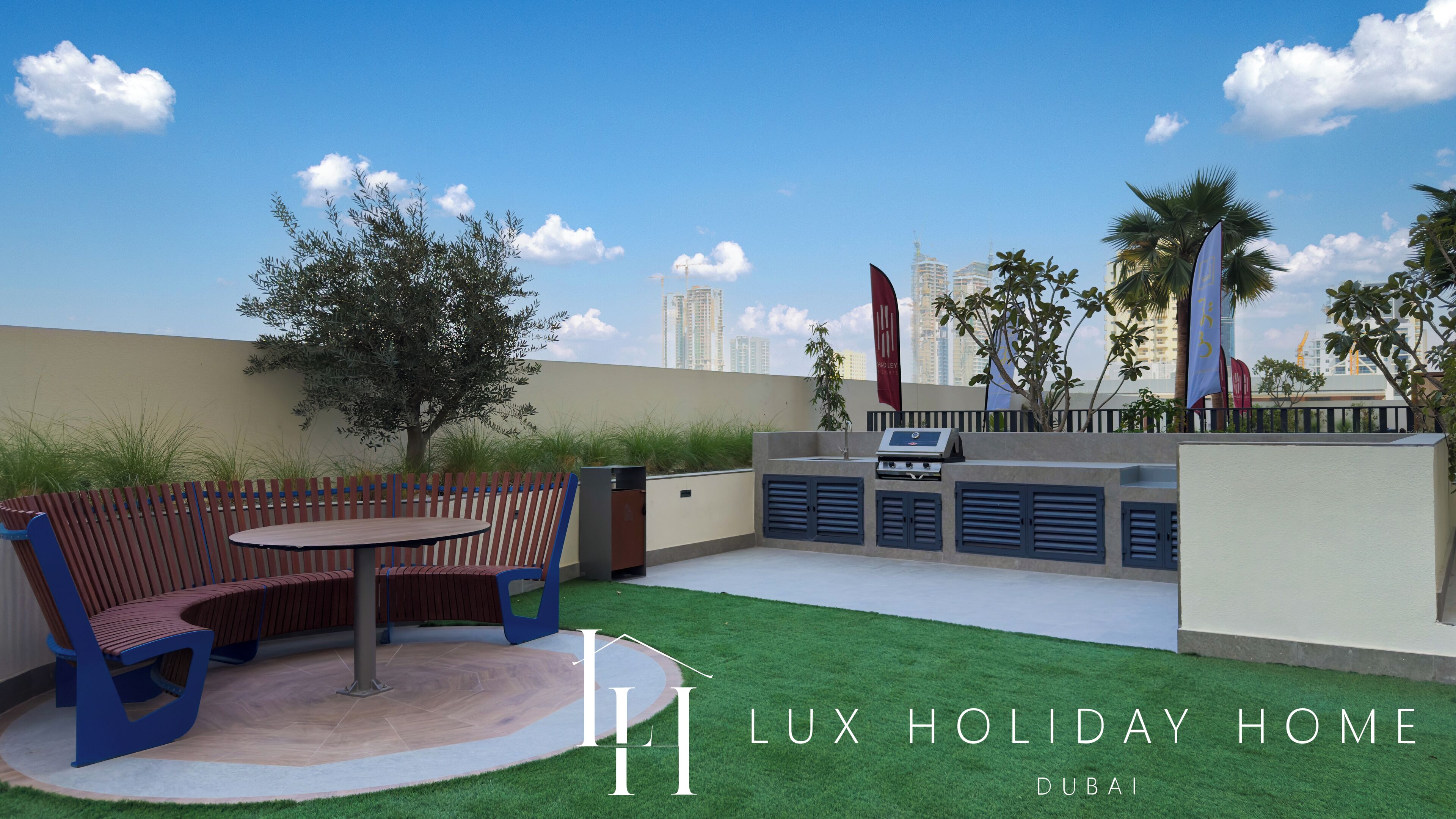 A patio area with a round table and benches, a grill, and a view of Dubai's skyline.