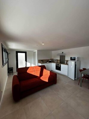A modern apartment with a living area featuring a red sofa, a kitchen with white cabinets, and a dining area with a table and chairs.