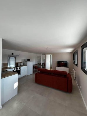 A modern kitchen with white cabinetry, a red sofa, and a large window.