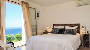 A bedroom with a large bed, two bedside lamps, a nightstand, and a view of the sea through a glass door. - Vacation home Babo by Interhome (Porto Vecchio)