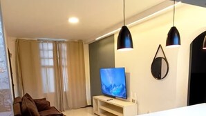 A modern living room with a sofa, TV, and pendant lights. - 2 bed apart in Asa Sul • Premium Location • Next Esplanada, Lake, Parks, Airport (Brasília)