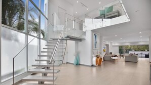 Un interior moderno con una escalera de cristal, una sala de estar con sofás y un comedor.