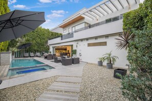 A modern outdoor pool area with lounge seating and umbrellas, surrounded by a pebble garden and potted plants. - Colgate Vantage - The House of Views Rooftop Deck & Hollywood Hills Vistas (Los Angeles)