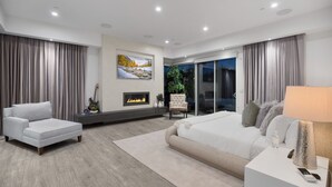 Un dormitorio moderno con sofá, cama, chimenea y vistas al exterior.