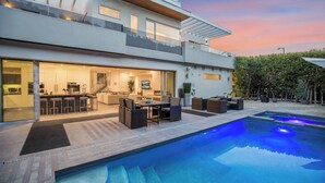 Una casa moderna de dos pisos con cocina y comedor integrados, una piscina y un patio con mobiliario exterior.