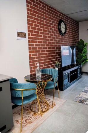Een woonkamer met een bakstenen muur, een ronde tafel met stoelen, een flatscreen televisie en een potplant.