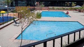 A swimming pool area with two pools, a covered seating area, and a building with a dark roof. - The space is deigned with comfort, peace and easy living in mind. (Midrand)