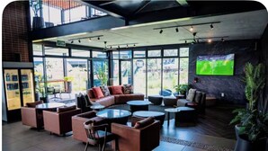 A modern lounge area with leather sofas, round tables, and a large TV screen on the wall. - The space is deigned with comfort, peace and easy living in mind. (Midrand)