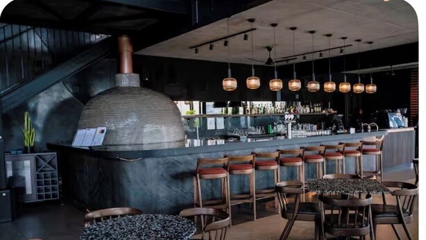 A bar area with a large pizza oven, wooden chairs, and a bar counter. - The space is deigned with comfort, peace and easy living in mind. (Midrand)