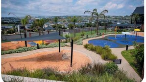A landscaped outdoor area with a pool, palm trees, and a view of a residential area. - The space is deigned with comfort, peace and easy living in mind. (Midrand)