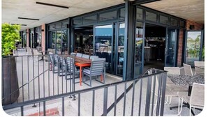 An outdoor patio area with tables and chairs, glass doors leading to an interior space, and a view of the surrounding area. - The space is deigned with comfort, peace and easy living in mind. (Midrand)