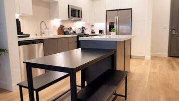 A modern kitchen with white cabinetry, stainless steel appliances, a central island, and a dining area with a bench.