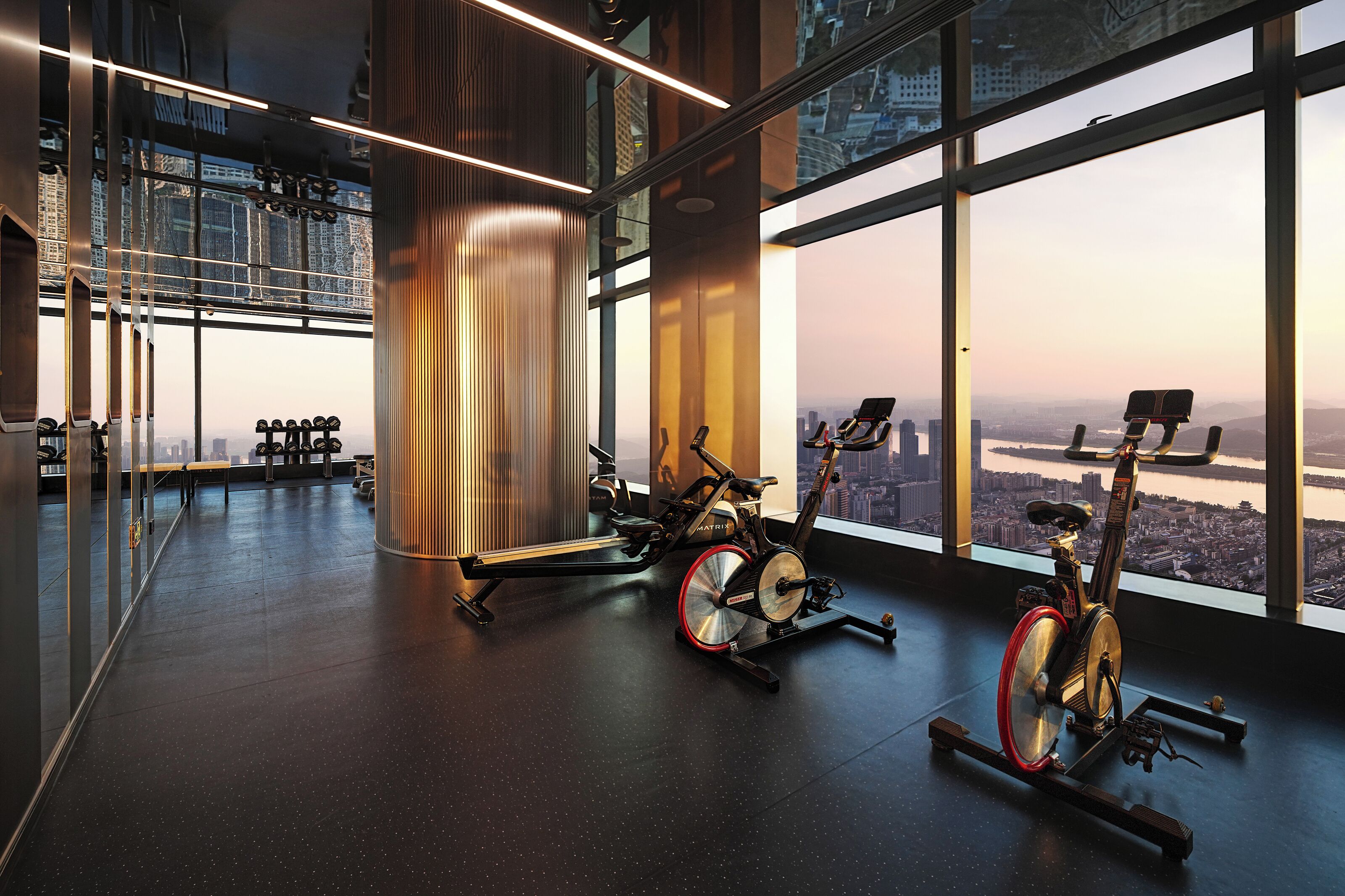 A modern gym with stationary bikes and a large window offering a city view.