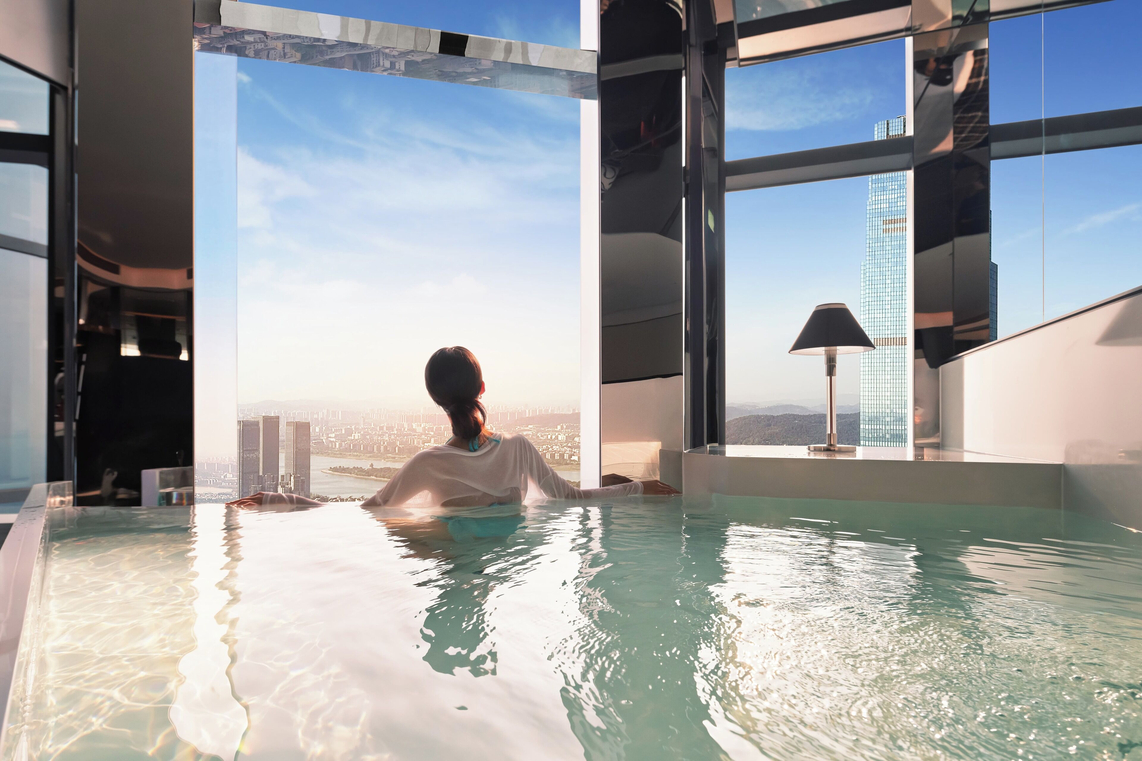 Una persona en una piscina interior moderna con ventanas amplias y vista a la ciudad.