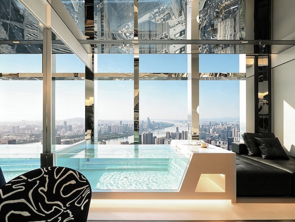 A modern interior with a glass infinity pool, a city view, and a seating area.