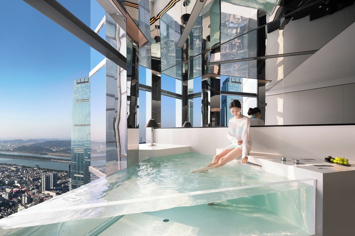 A modern interior with a glass infinity pool, a city view, and a high-rise building in the background.