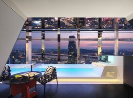 Una habitación moderna con vista panorámica de la ciudad, una mesa de vidrio con una silla y un pequeño área de piscina.