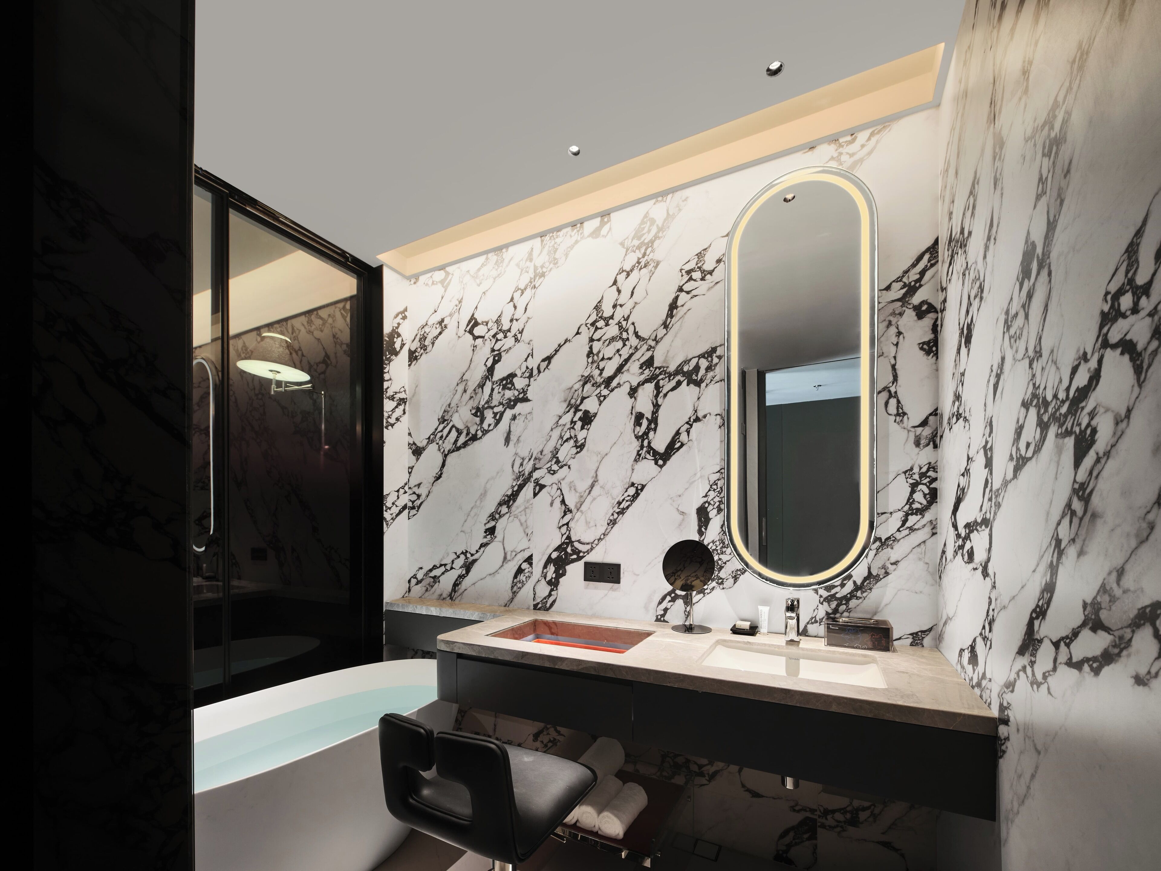 A modern bathroom with a marble backsplash, a large mirror, a bathtub, and a vanity with a sink.