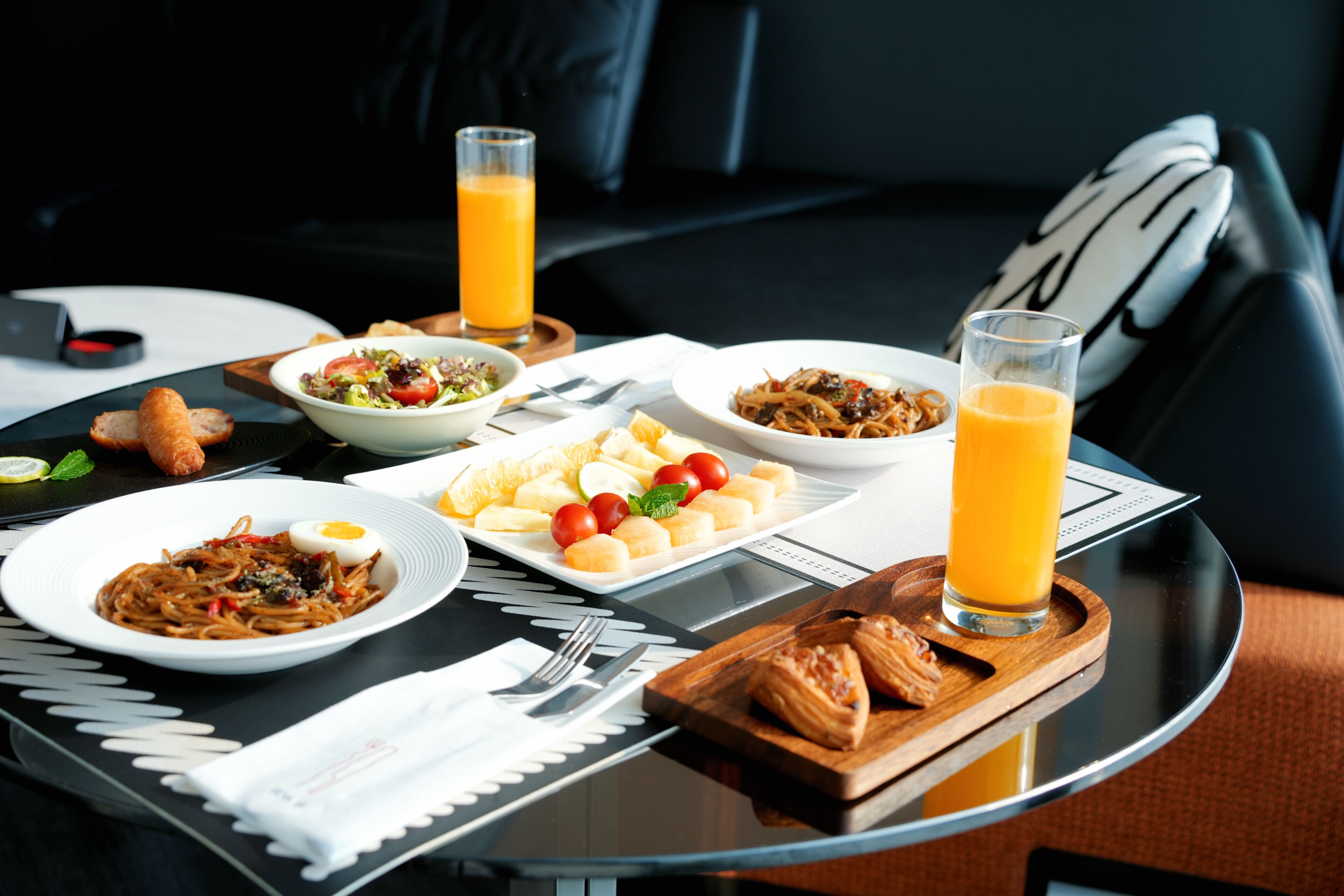 A breakfast setting with various dishes, a glass of orange juice, and a laptop on a table.