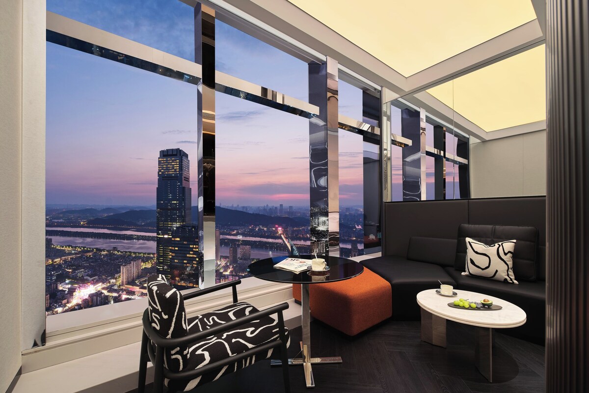A modern room with a large window, a sofa, a small table, and a chair.