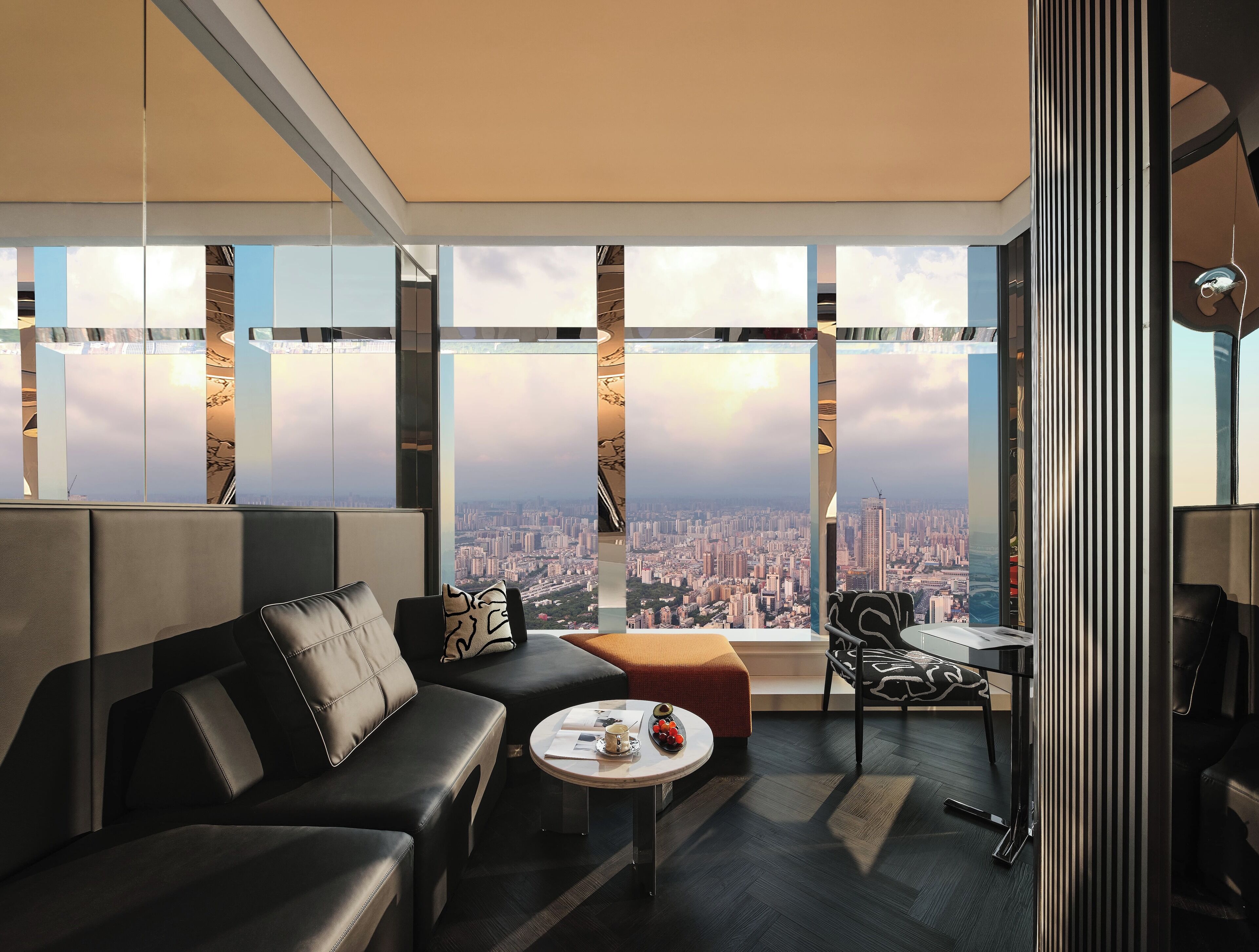 Ein modernes Interieur mit einer Couch, einem Couchtisch und Blick auf eine Stadtkulisse durch große Fenster.