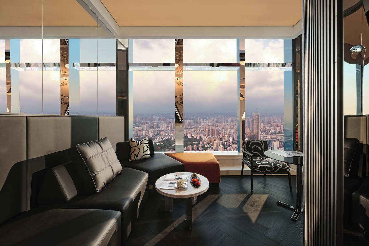 A modern interior with a sofa, coffee table, and a view of a cityscape through large windows.