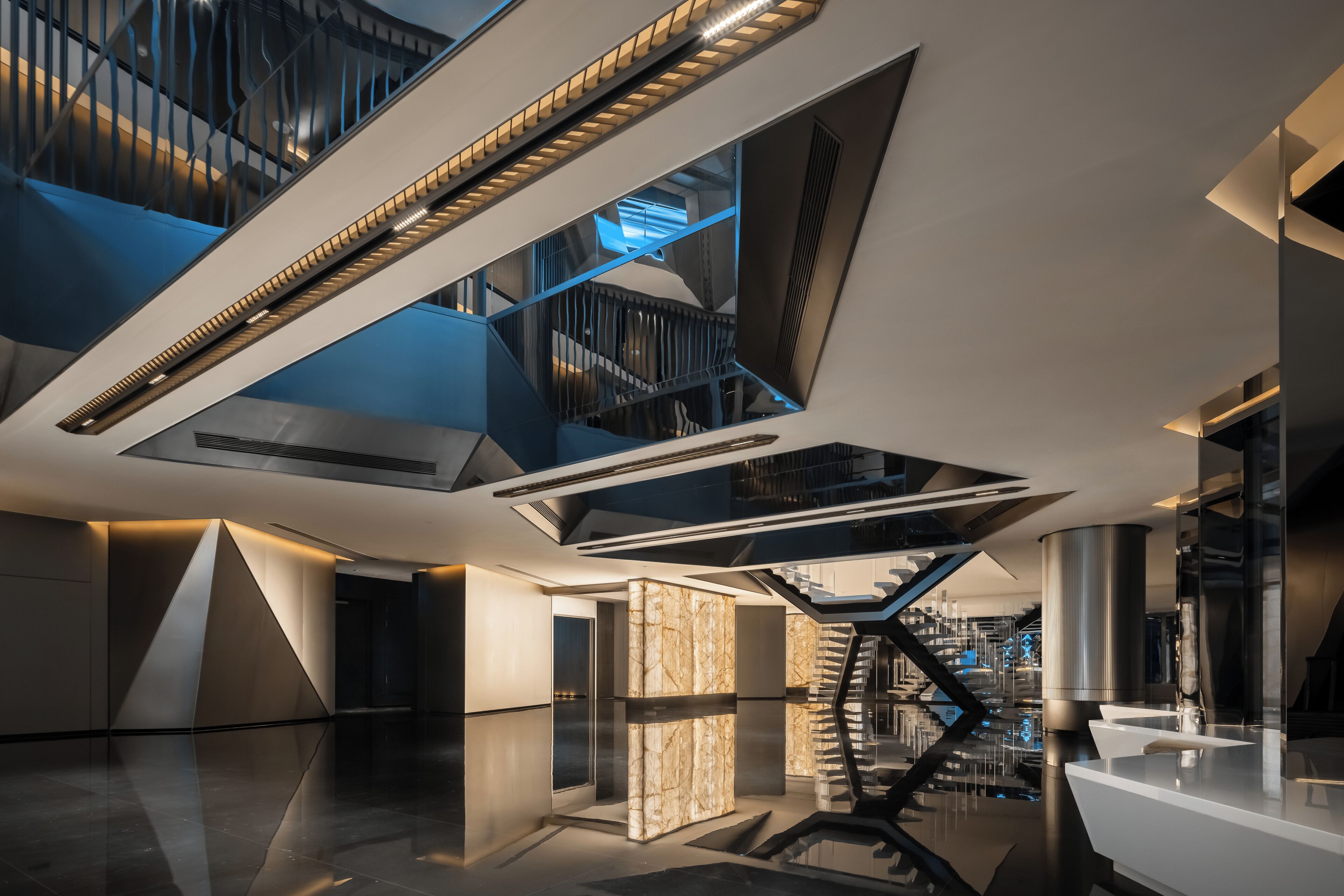 Un interior moderno con una escalera central, superficies reflectantes y elementos arquitectónicos geométricos.