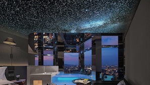 Una habitación de hotel moderna con techo que simula un cielo estrellado, vistas a la ciudad, una cama, un escritorio y una pequeña zona de piscina.