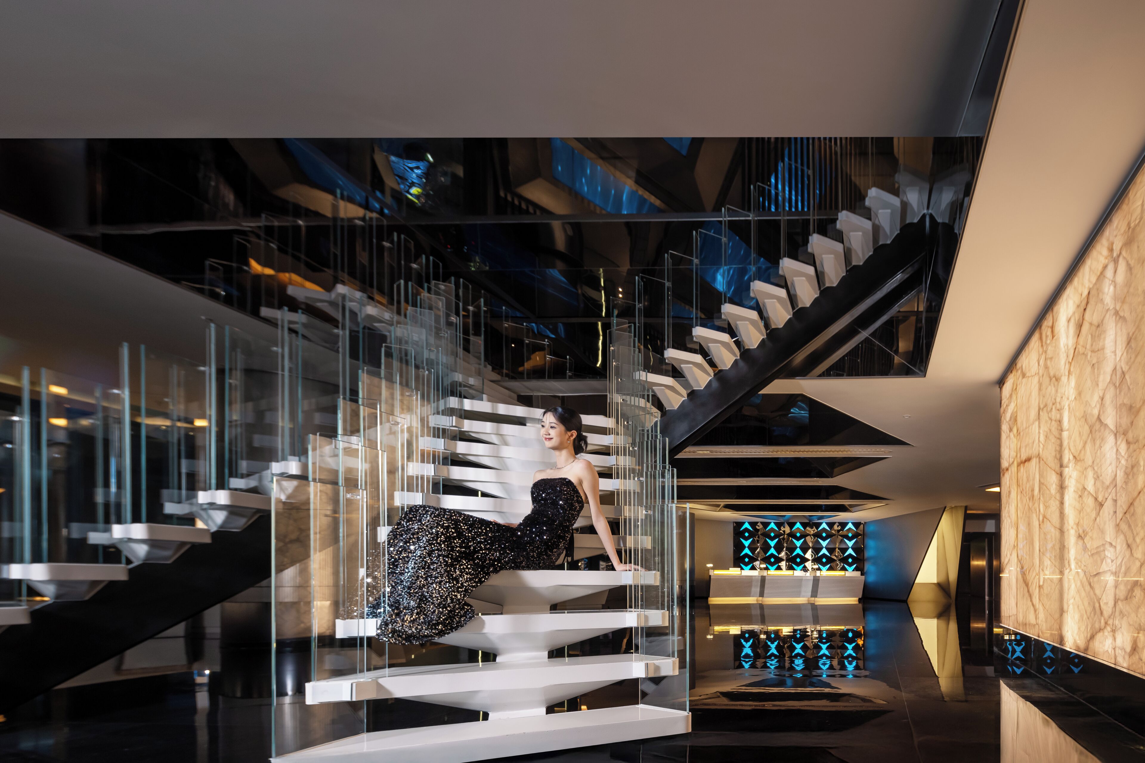 A modern interior with a glass staircase, a marble wall, and a geometric light pattern.
