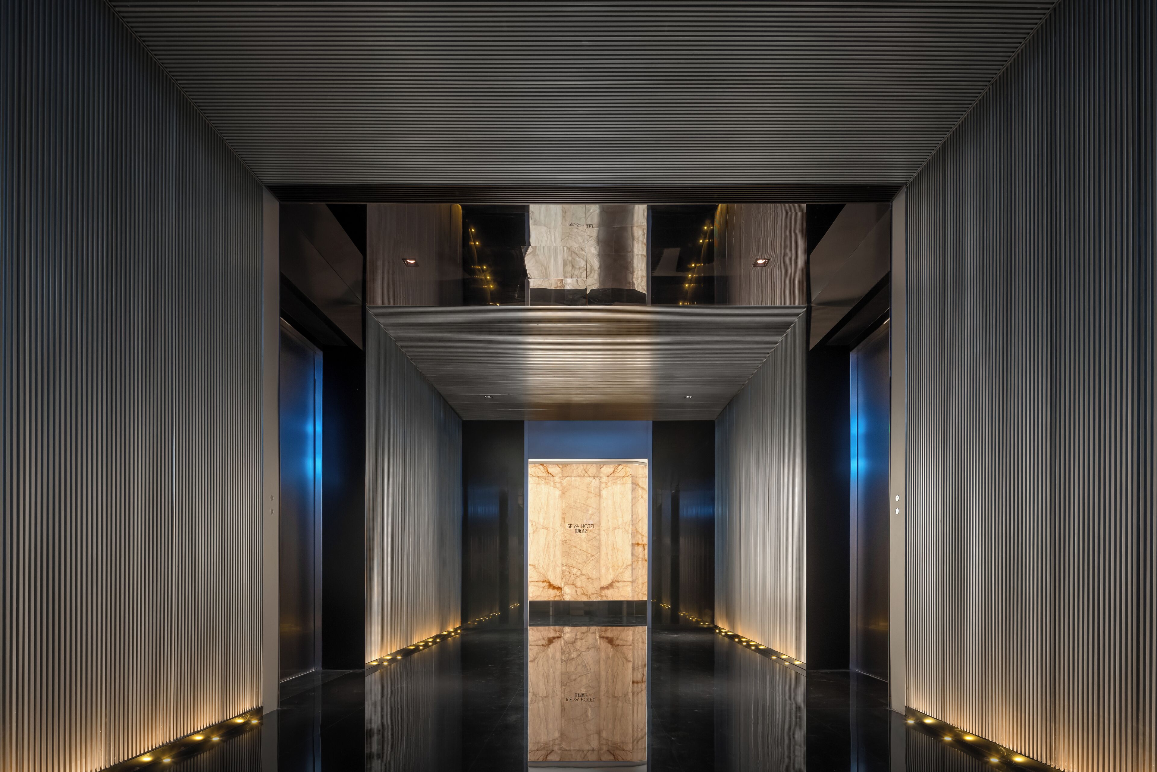 A modern hallway with a central marble column, flanked by vertical paneling and recessed lighting.