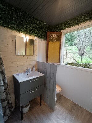 A bathroom with a wooden vanity, a mirror, a window with a view of greenery, and a toilet.